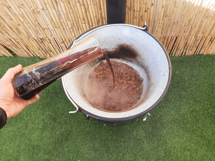 se ve una mano virtiendo vino tinto de un jarron en el guiso, durante la preparacion de la receta del goulash eslovaco a la leña
