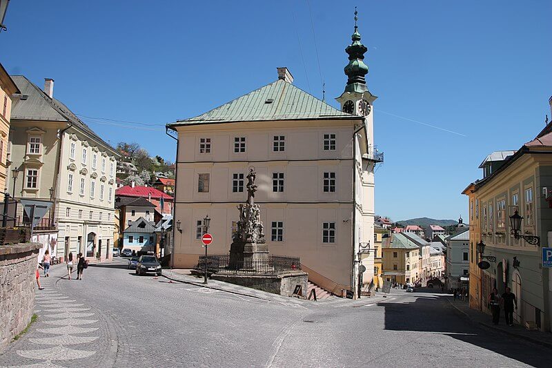 foto del centro de banska stiavnica en que se ve una bifurcacion de dos calles y una estatua en el centro de la misma