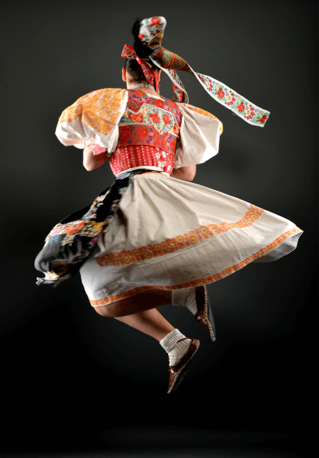 tradiciones y folklore de eslovaquia: chica de espaldas vestida con un vestido tradicional blanco naranja y rojo girando en el aire en pleno salto con fondo negro