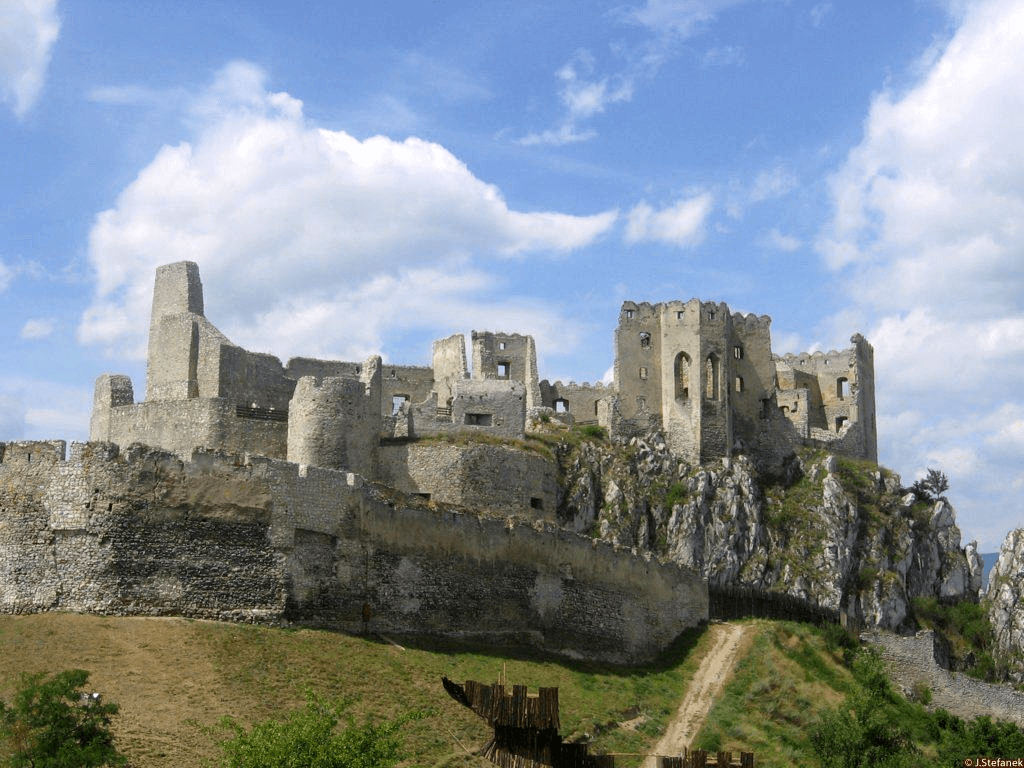 las ruinas del castillo de becko o hrad beckov vistas de frente a lo alto de una colina rocosa con un cielo azul claro y algunas nubes blancas