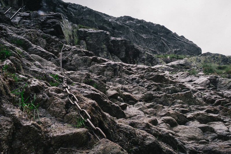 foto en contrapicado de una montana rocosa en que se ve una cadena y una escalera que forman parte de una via ferrata