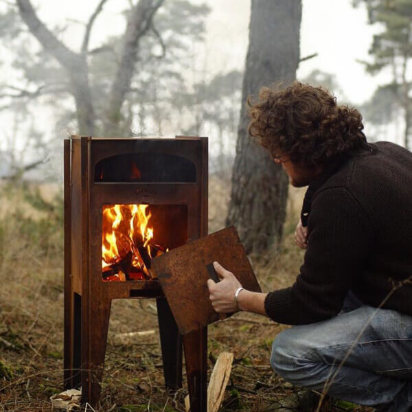 hombre en el bosque con un horno de lena para exterior encendido