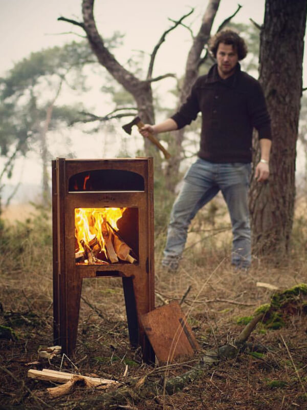 hombre en el bosque con un hacha y un horno de lena para exterior encendido