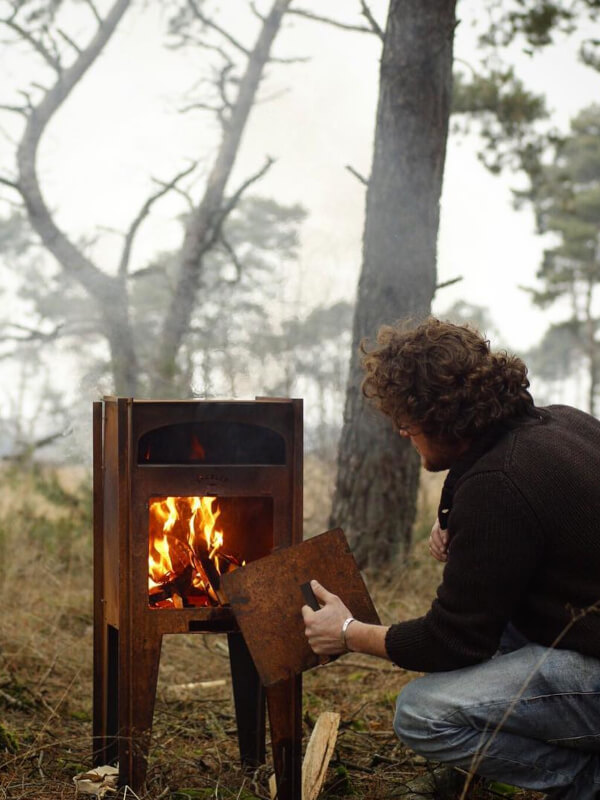 hombre en el bosque con un horno de lena para exterior encendido
