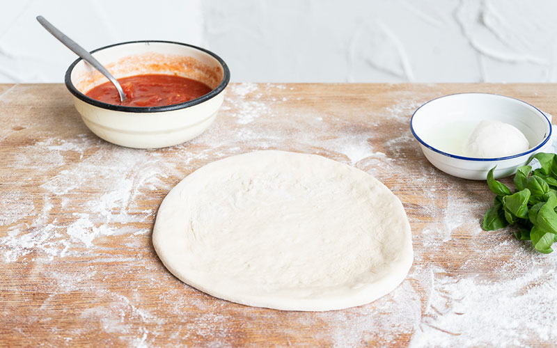 masa de pizza ya en forma redonda en una tabla llena de harina