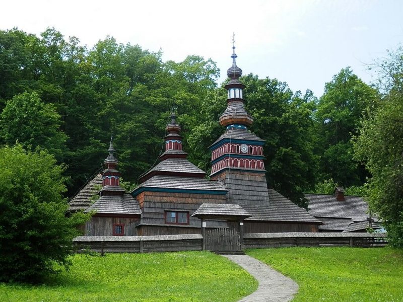 vista desde fuera del museo al aire libre de bardejov en que se ve una de las iglesias de madera en medio del frondoso y verde bosque