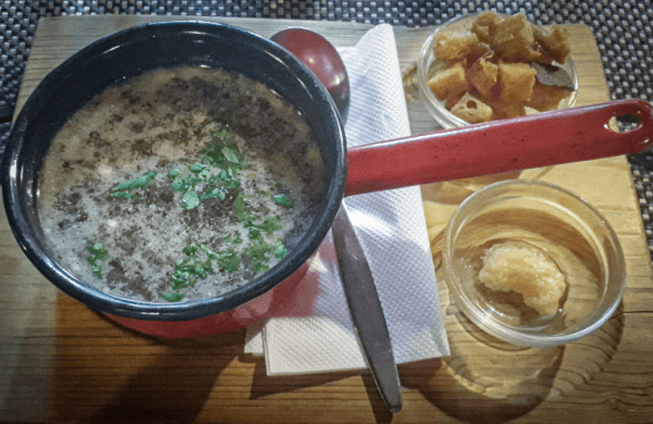 gastronomia y platos tipicos de eslovaquia: sopa de ajo servida directamente en un cazo en una tabla de madera con un bol con extra ajo picado y picatostes